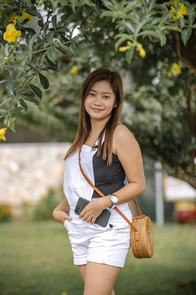 Woman wearing a white sleeveless dress, holding a brown leather bag
